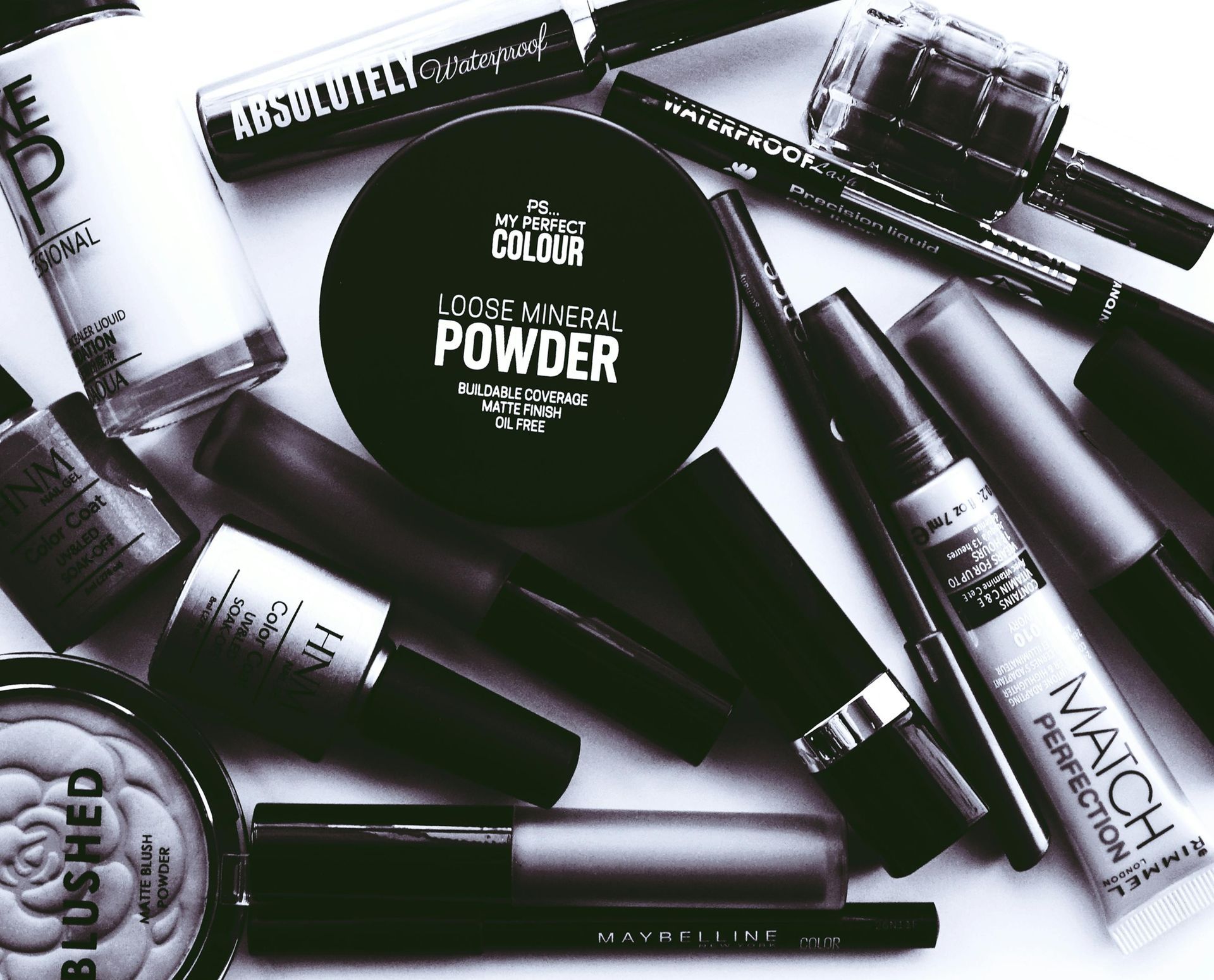 A mixed variety of  cosmetics are sitting on a table in black and white.