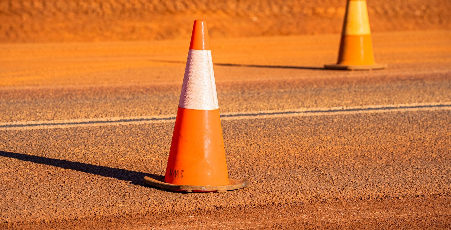 Two orange and white traffic cones are sitting on the side of a road.