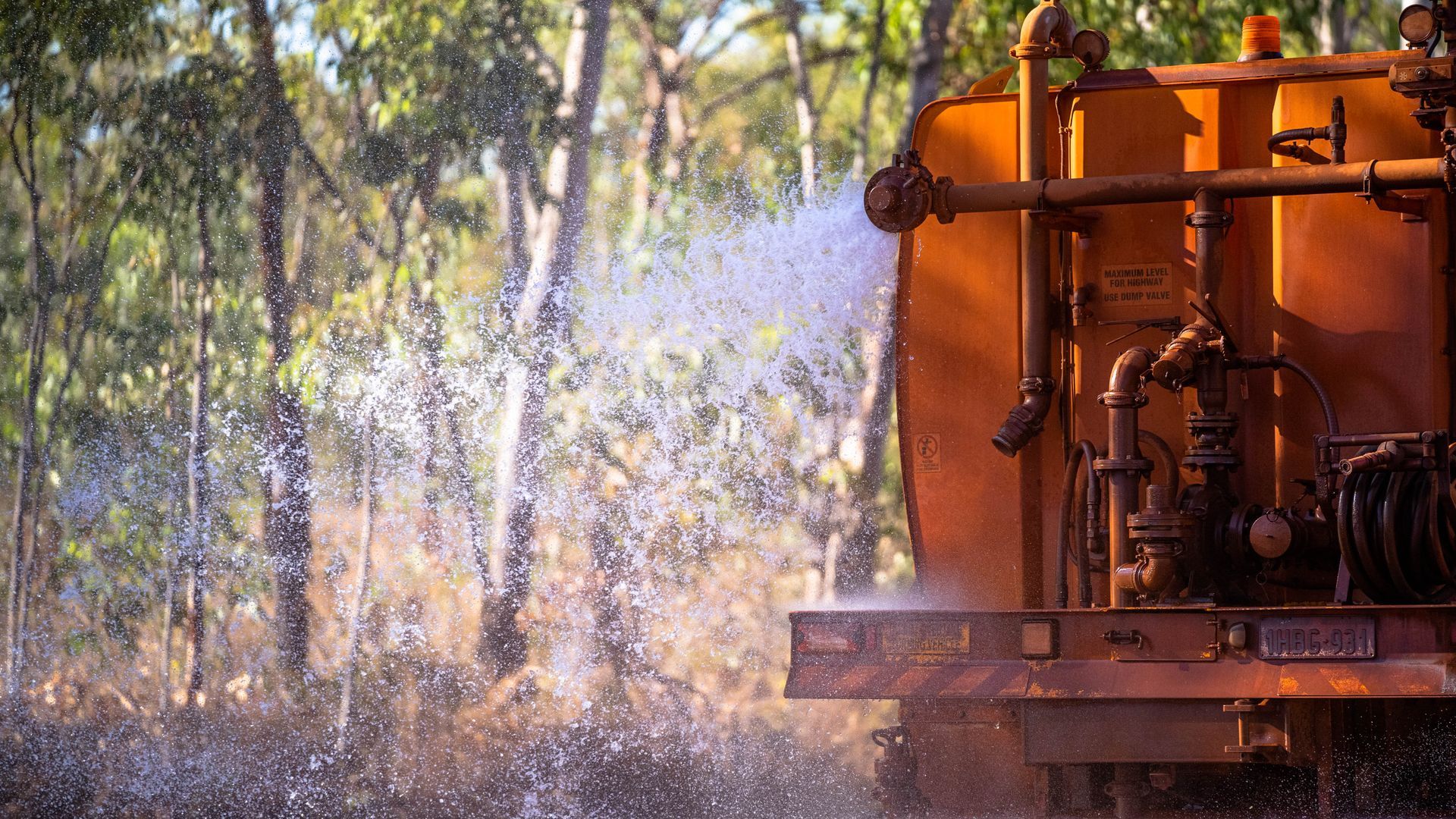 A truck is spraying water on a forest with trees in the background.