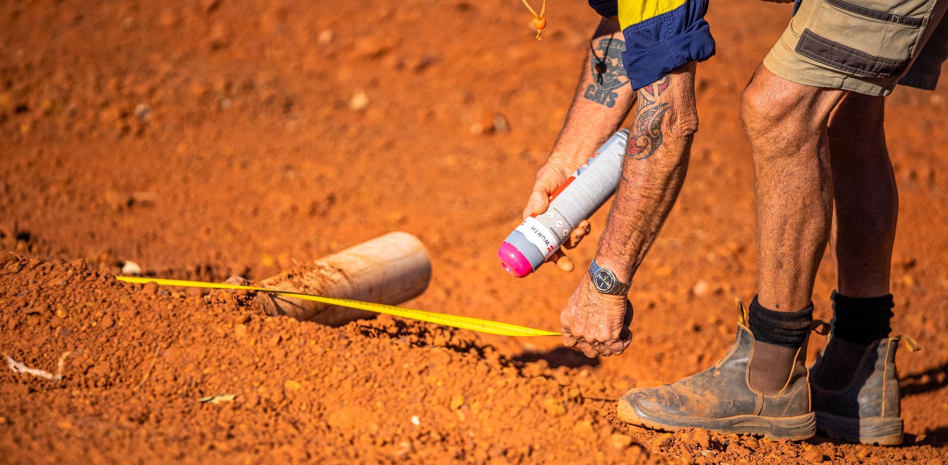 A man is measuring a hole in the ground with a tape measure.