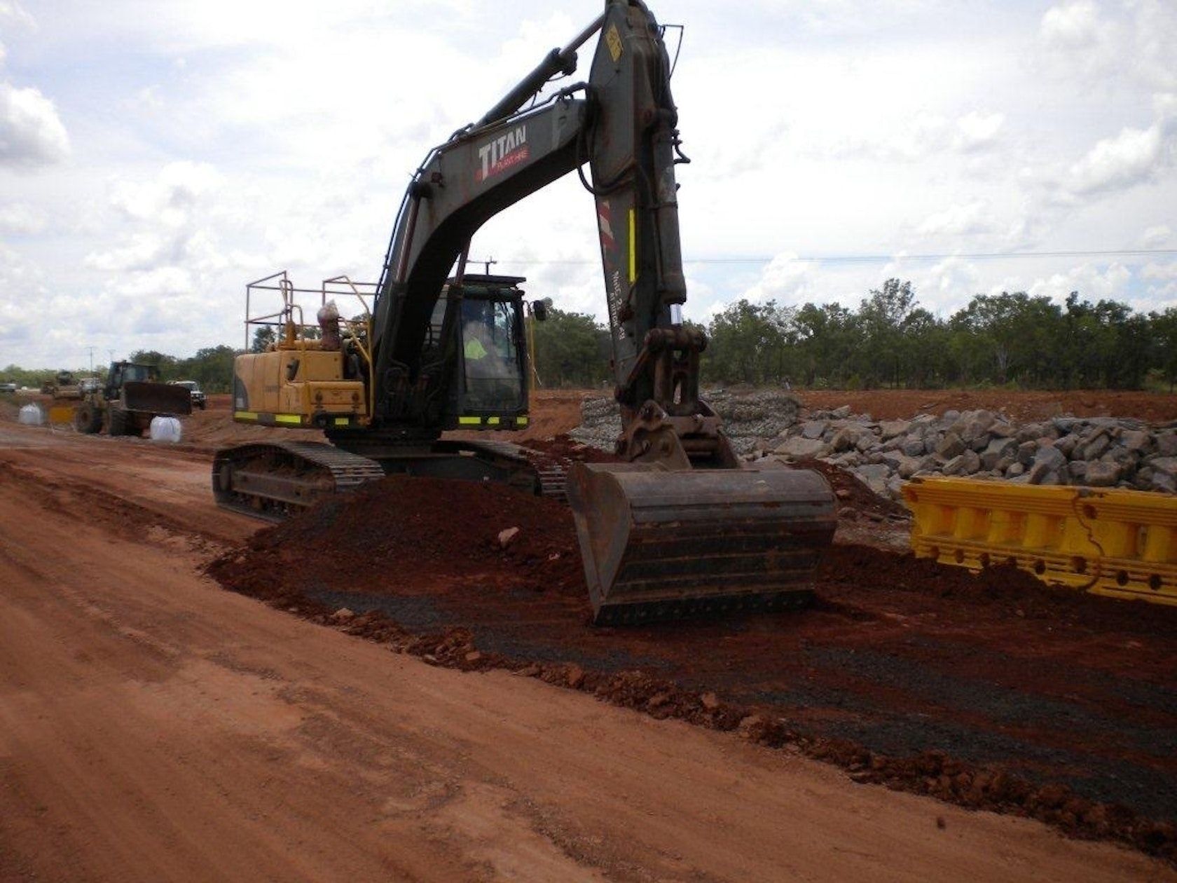 A large excavator is moving dirt on a dirt road.