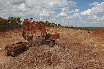 An excavator is loading a dump truck with dirt in a dirt field.