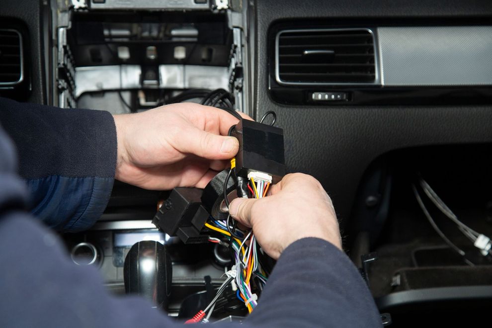 Mani che lavorano sui cavi dell'auto, sullo sfondo il cruscotto.