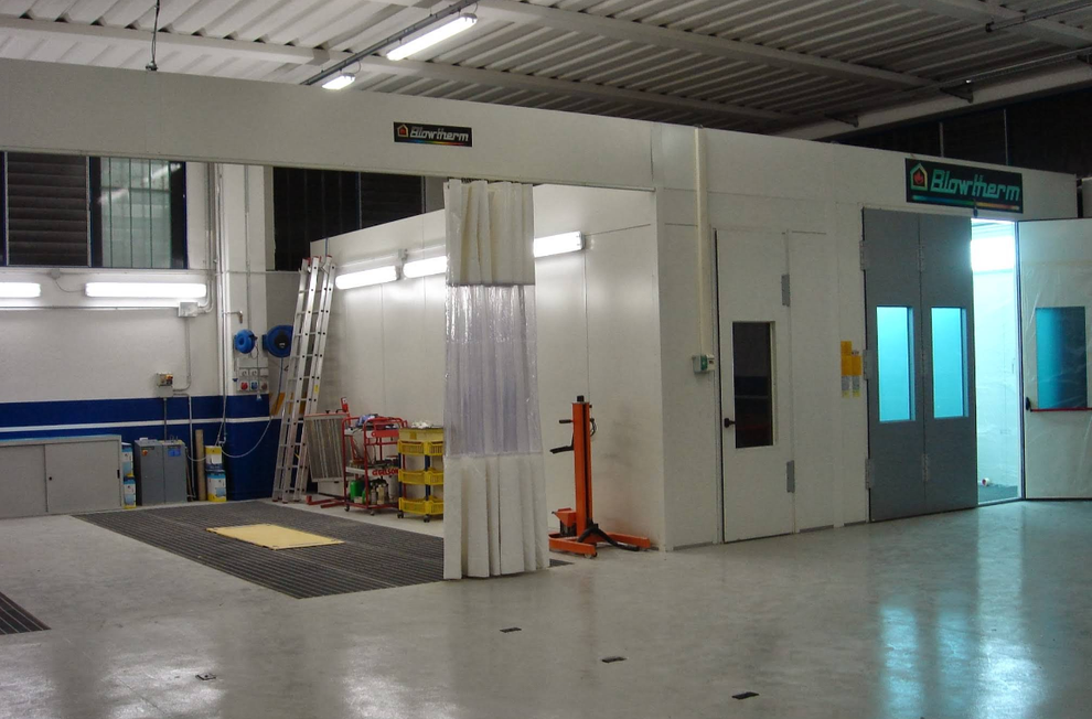 Cabina di verniciatura a spruzzo in un garage. Pareti, porte e illuminazione dall'alto bianche. Scala e attrezzatura all'interno.