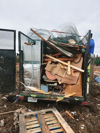 Trailer overflowing with construction debris, including wood, cardboard, and wire mesh, at a waste disposal site.