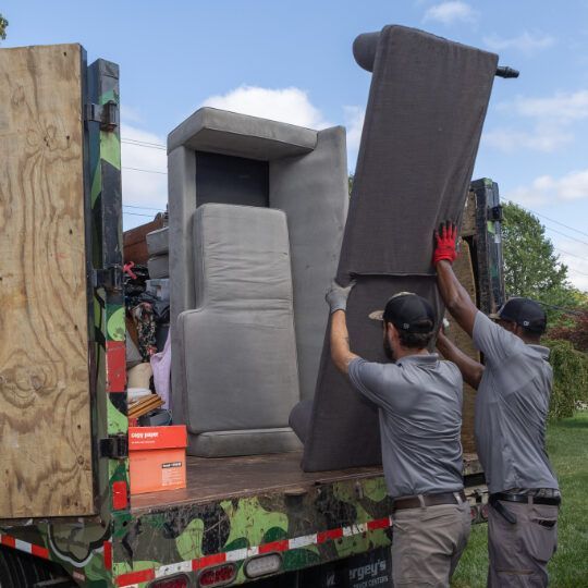 Two people loading gray furniture into a truck.
