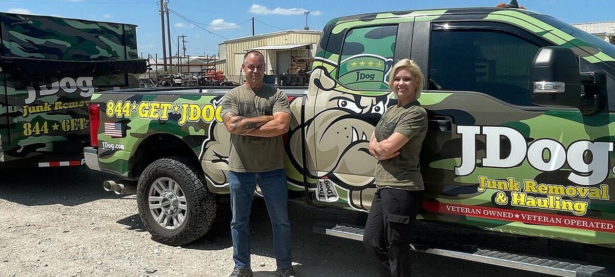 Two people stand next to a camouflage truck and trailer. The truck has 