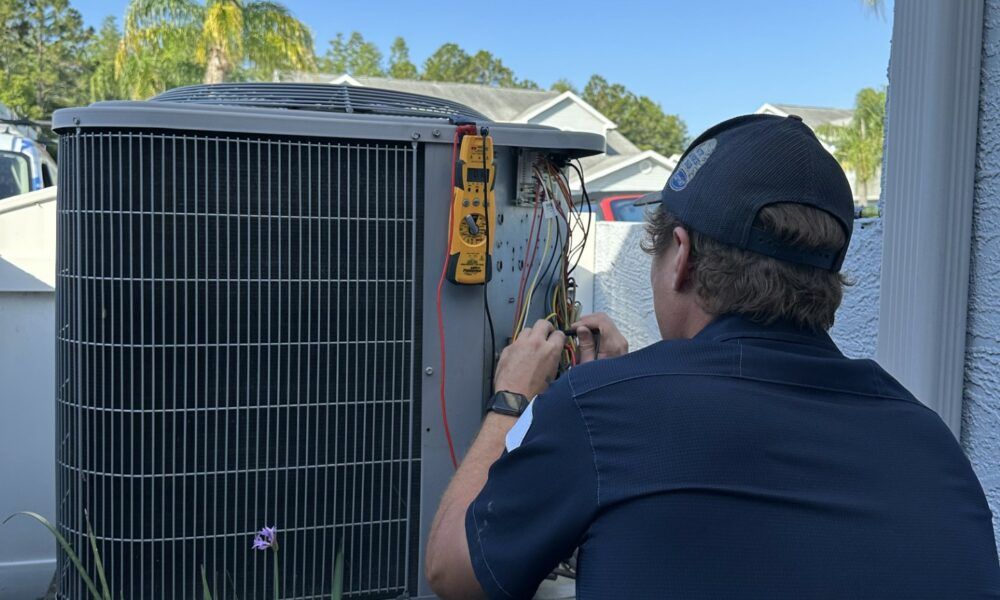HVAC technician working on an air conditioner unit outside a house on a sunny day.