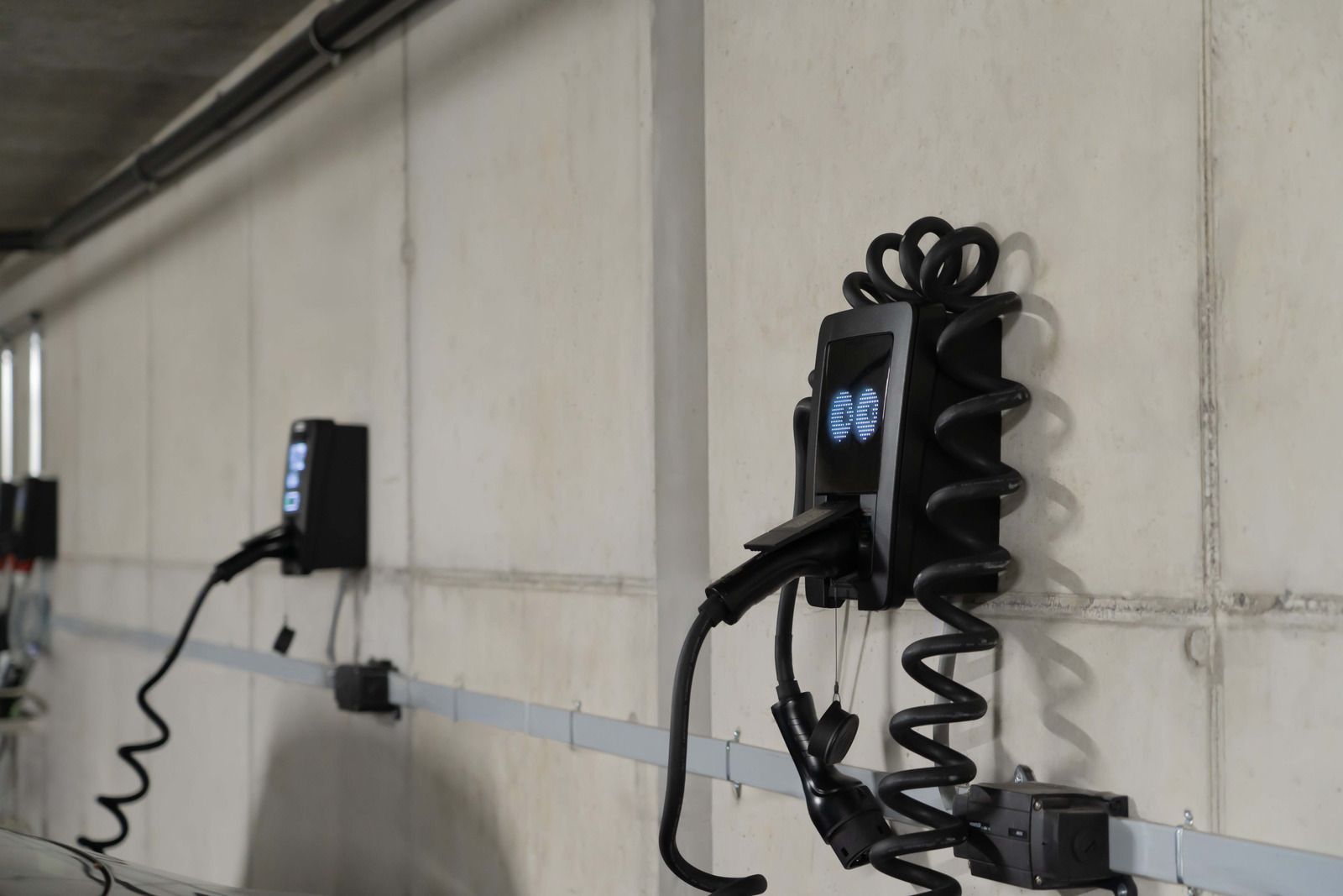 Electric vehicle charging stations mounted on a light-colored wall, with coiled black charging cables.
