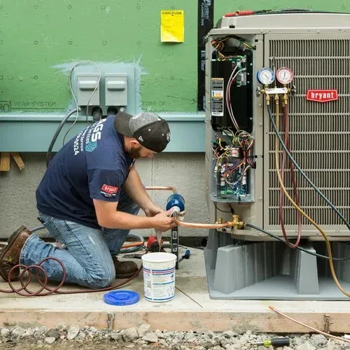 HVAC technician kneels, connecting copper tubing to a Bryant air conditioning unit outdoors.