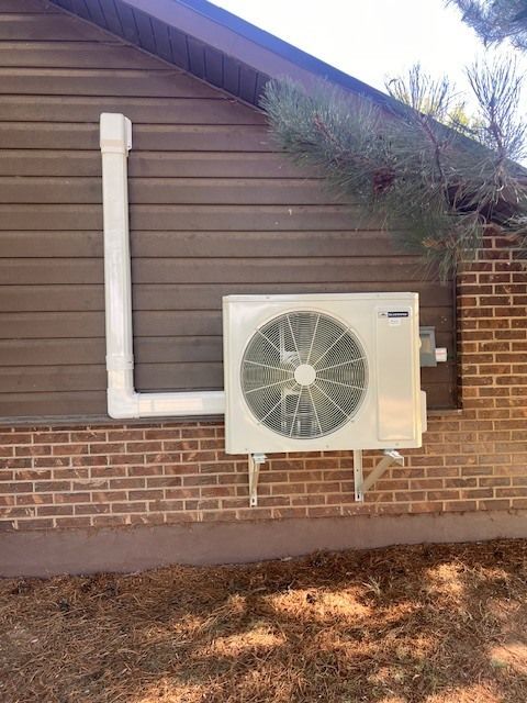 Outdoor air conditioning unit attached to a brick wall with white exhaust pipe.