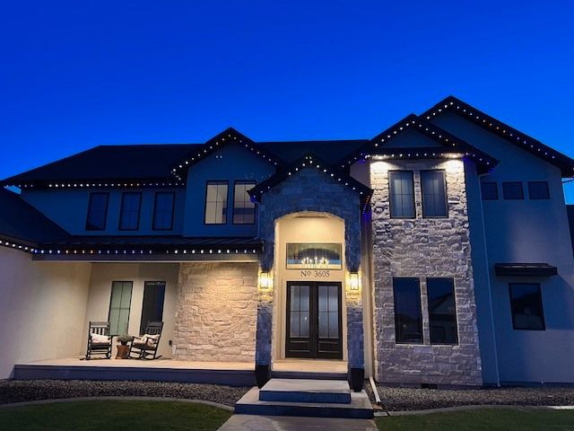 Night view of a house with decorative lights along the roofline and over the front door.