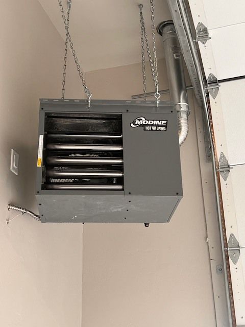 Gray ceiling-mounted garage heater with exhaust pipe and chains, near a garage door.