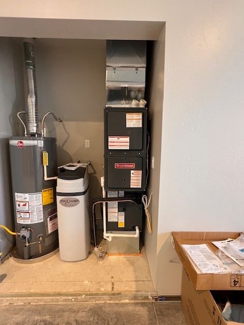 Water heater, furnace, and water softener in a utility closet with gray walls and a cardboard box.