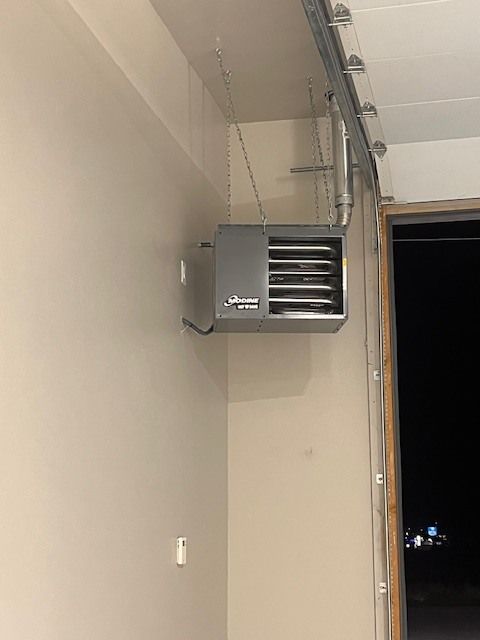 A gray garage heater mounted on a tan wall near a garage door.