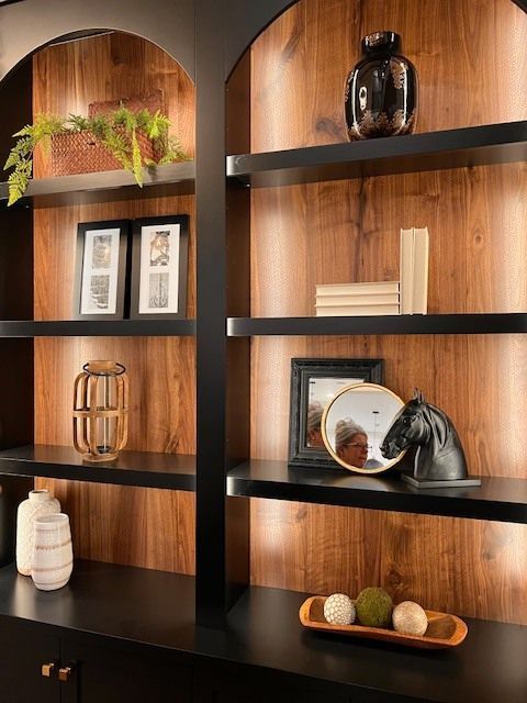 Built-in bookshelf with black shelves and dark wood backing, displaying decor like vases and framed photos.