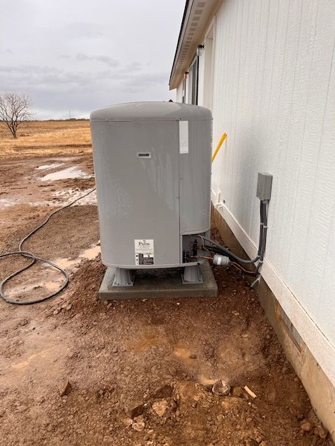 Large gray water tank next to a white building. Electrical box and yellow pipe visible. Outdoor setting.
