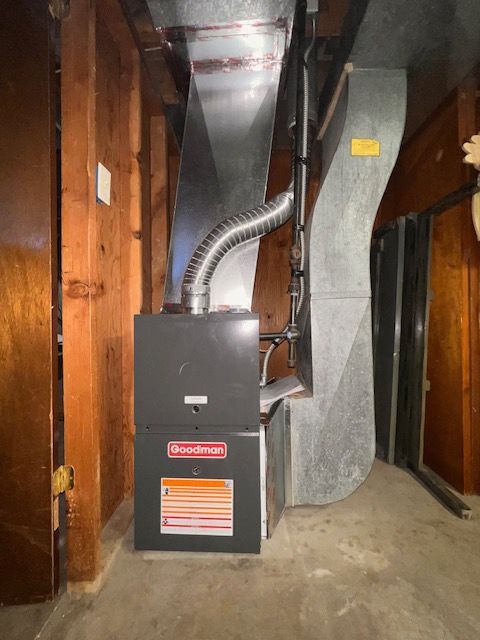 A Goodman furnace in a wooden-walled room with metal ductwork.