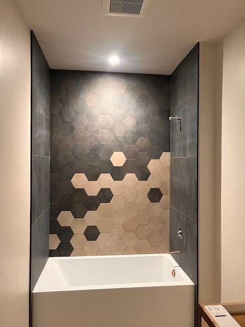 Bathroom with hexagon-tiled feature wall, bathtub, and shower fixture. Dark gray, tan, and white colors.