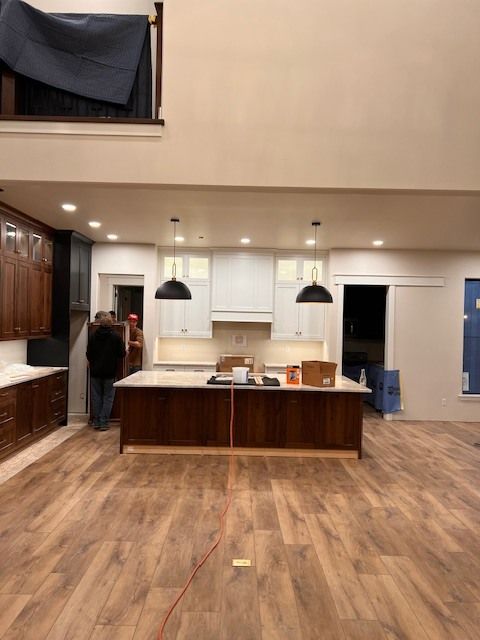 Spacious kitchen with a central island and dual-tone cabinetry. Two people are present, working.