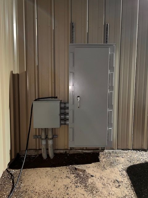 Gray metal door and electrical box mounted on a corrugated metal wall, with conduit running to the box.