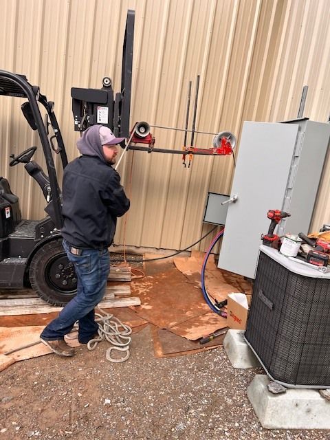 A person working on electrical equipment outside near a forklift and building.
