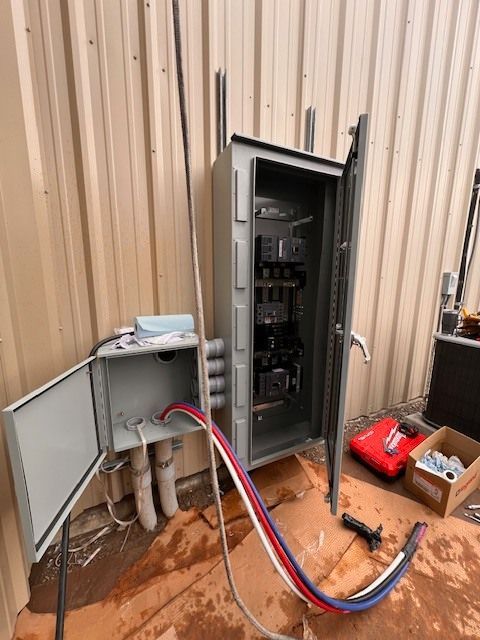 Electrical panel with open doors, wires and conduit, outdoors.