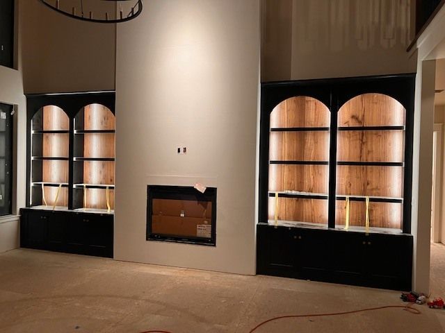 Built-in black bookshelves with arched tops flank a fireplace. 