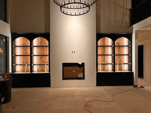 Built-in bookshelves flank a fireplace in a room under construction; warm wood interiors contrast with black framing.