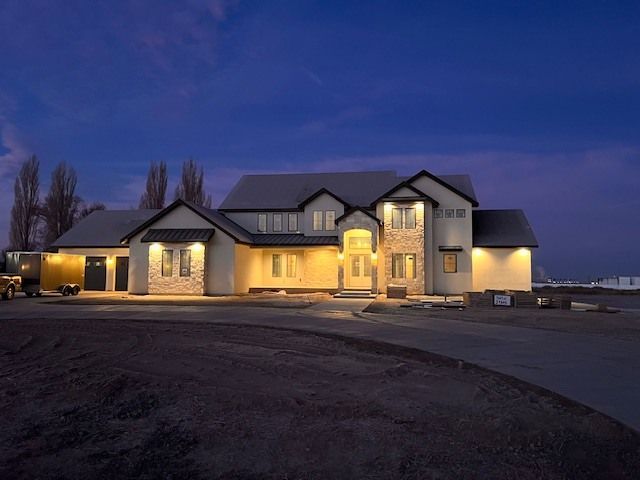 Large house at dusk with illuminated exterior, driveway, and dark blue sky.