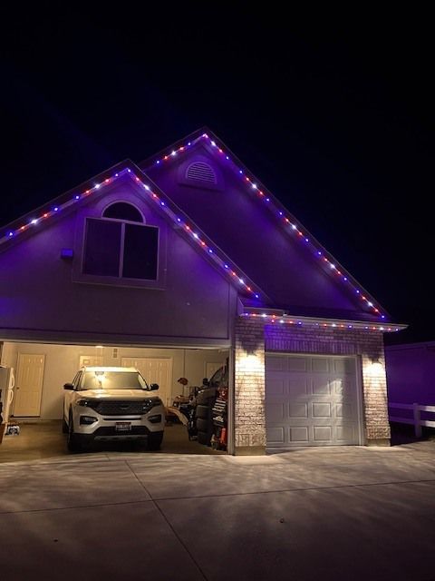 House with red and blue roofline lights, garage door closed, lit from within, car inside.