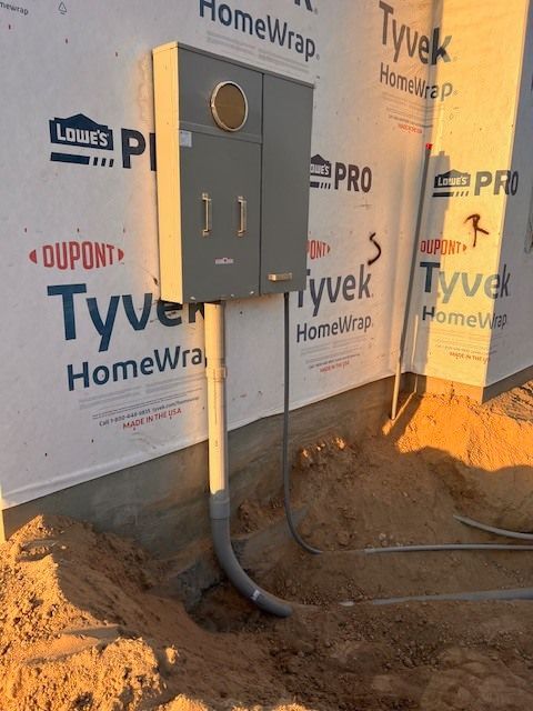 Gray electrical box installed on a building's exterior, with conduit running underground.