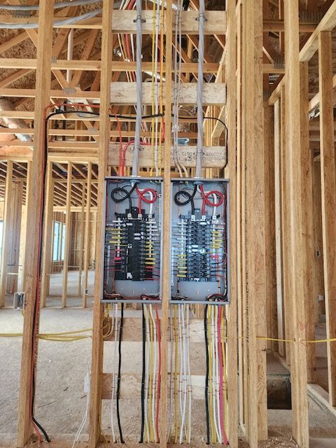 Two electrical panels mounted in wooden framing of a building under construction. Wires hang below.