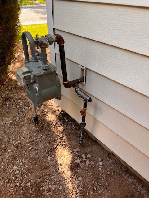 Gas meter and pipes attached to a white house exterior with brown gravel ground.