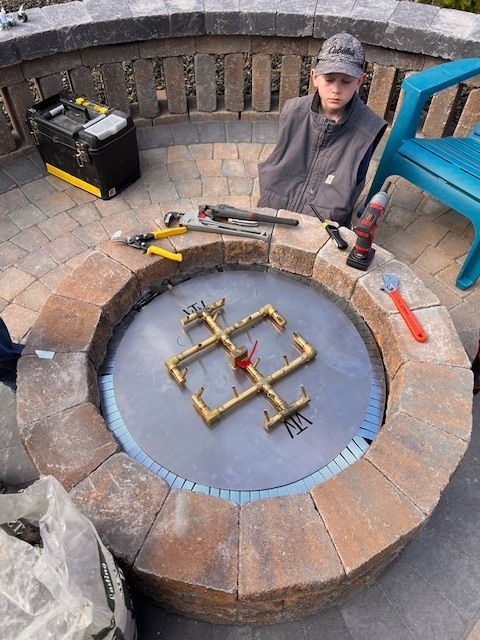 Person standing near a circular fire pit under construction with tools.