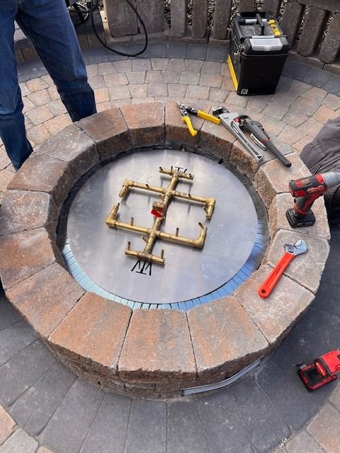 Fire pit being constructed with tools and gas burner assembly on a circular brick patio.