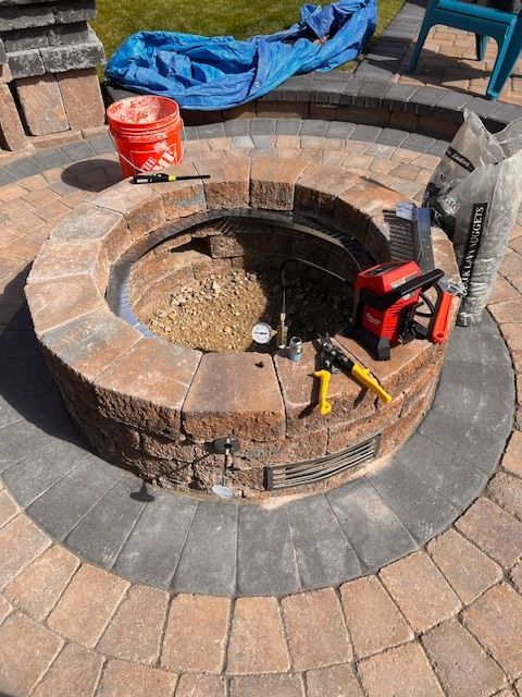 Fire pit construction: circular brick structure with tools, gravel, and a bag of material.