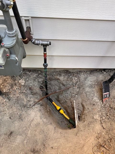 Gas meter and piping on a building exterior, with buried electrical wire and a shovel in the dirt.