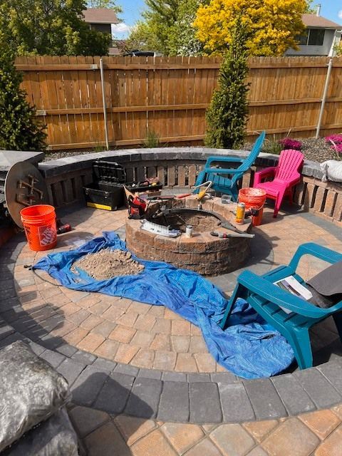 Patio with a stone fire pit, surrounded by chairs and building materials.