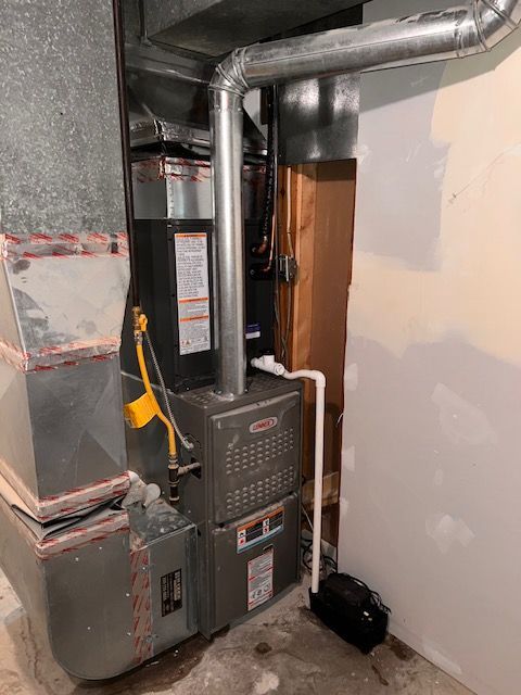 A furnace in a basement setting with metal ductwork and piping.