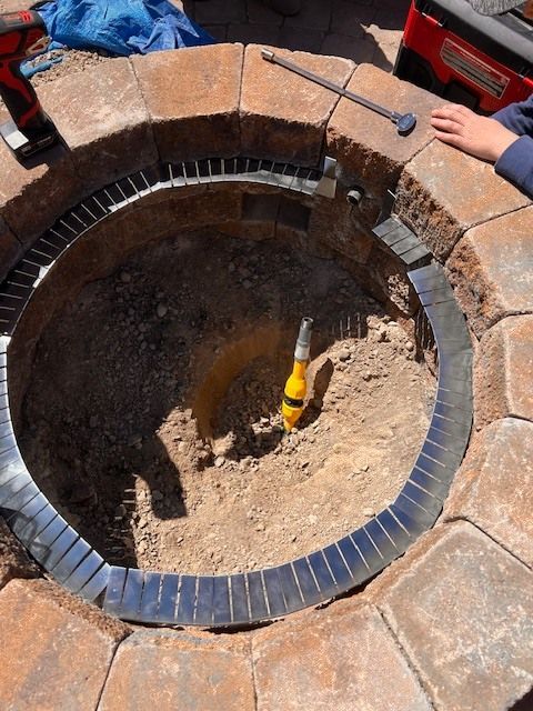 Fire pit construction in progress, circular brick structure, metal ring inside pit, tools nearby.