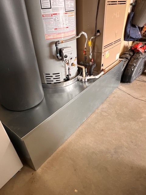 A metal pan sits beneath a water heater and furnace in a basement.