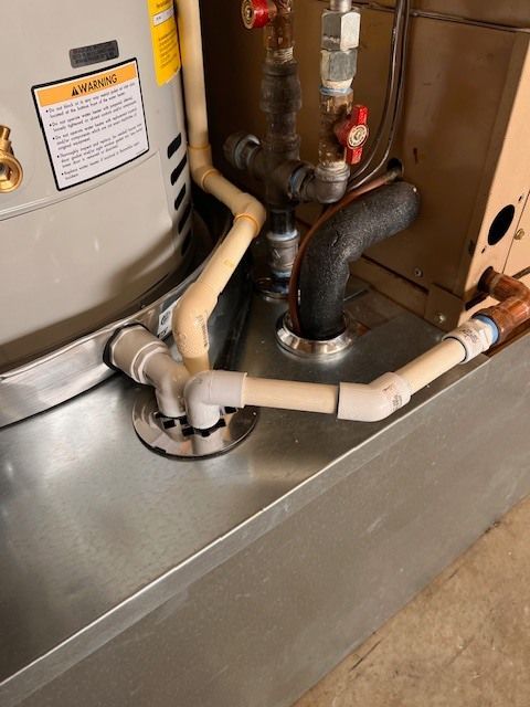 Plumbing connections near a water heater and furnace unit on a metal base. White and black pipes.