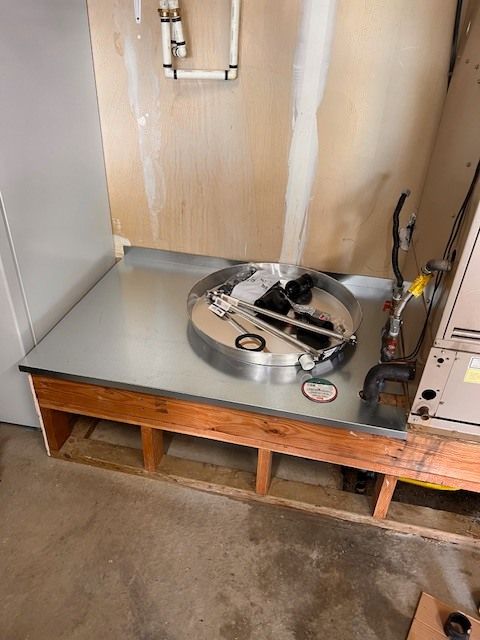 Metal tray on wooden base, pipes on wall, and HVAC unit in a utility room.