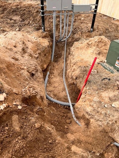 Trench with buried electrical conduits leading to electrical boxes. Dirt, utility pole, and a red marker visible.