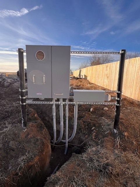 Gray electrical equipment installed near a wooden fence and dirt trench against a blue sky.