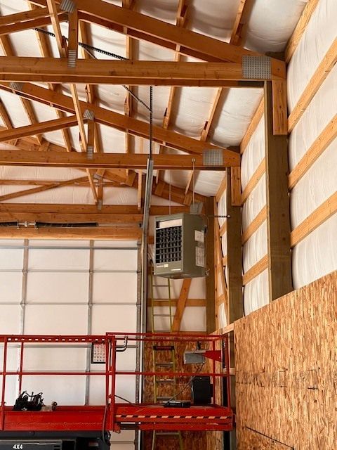 Interior of a large building with exposed wood beams and a suspended heater. A lift platform is in the foreground.