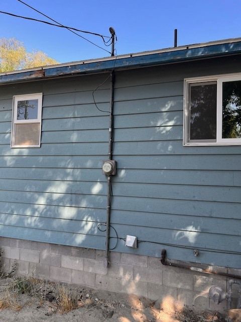 Blue siding of a house with windows, an electrical meter, and conduit attached.