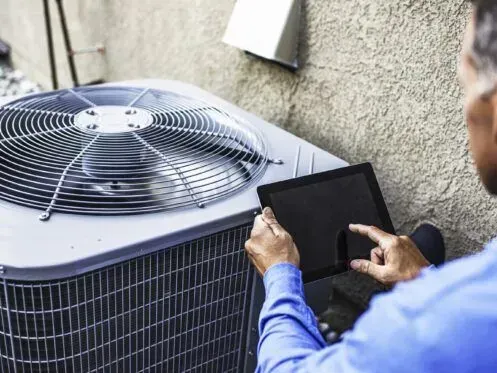 HVAC technician with a tablet inspecting an air conditioning unit.
