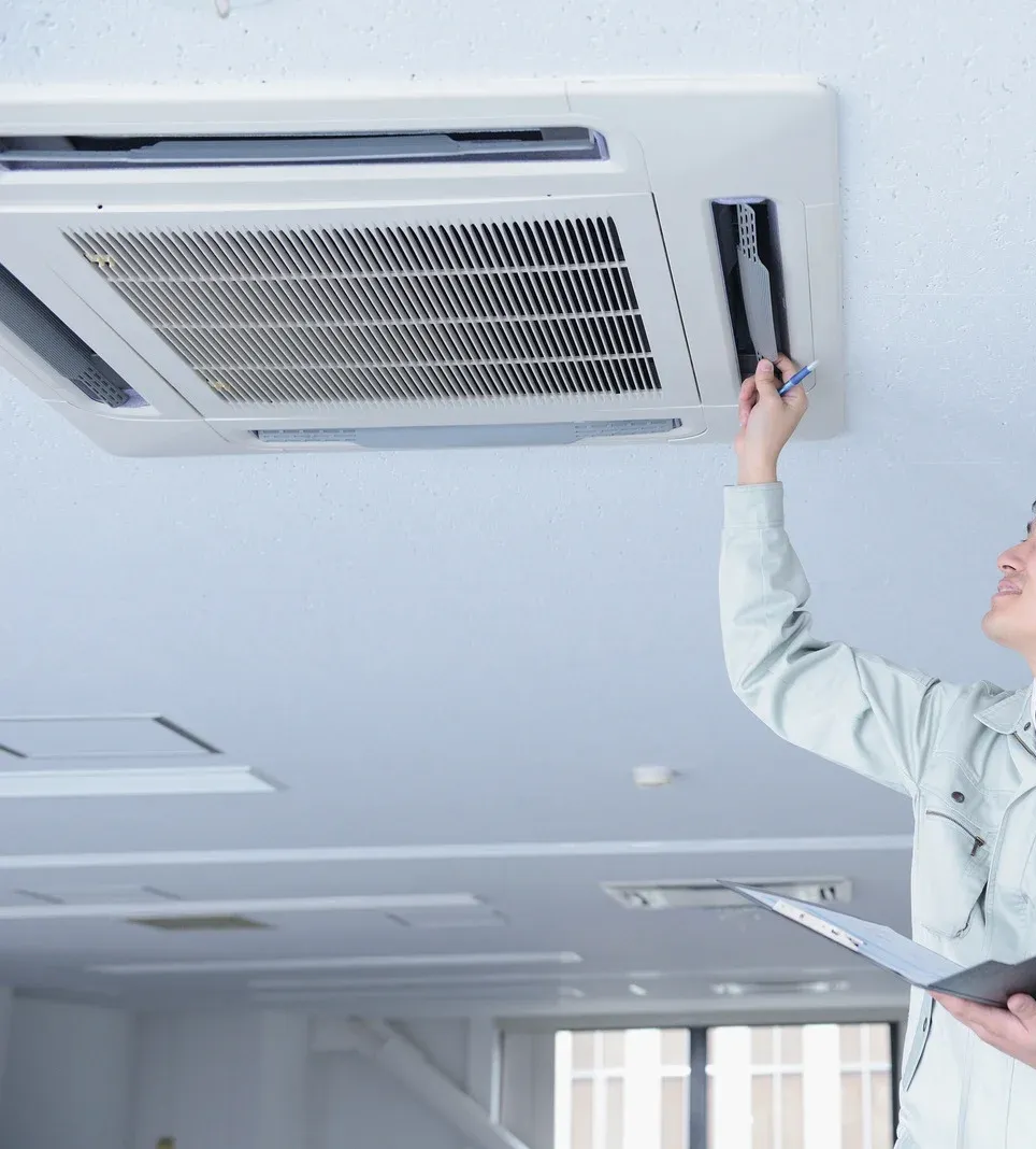 Technician inspecting ceiling-mounted air conditioner in office setting.